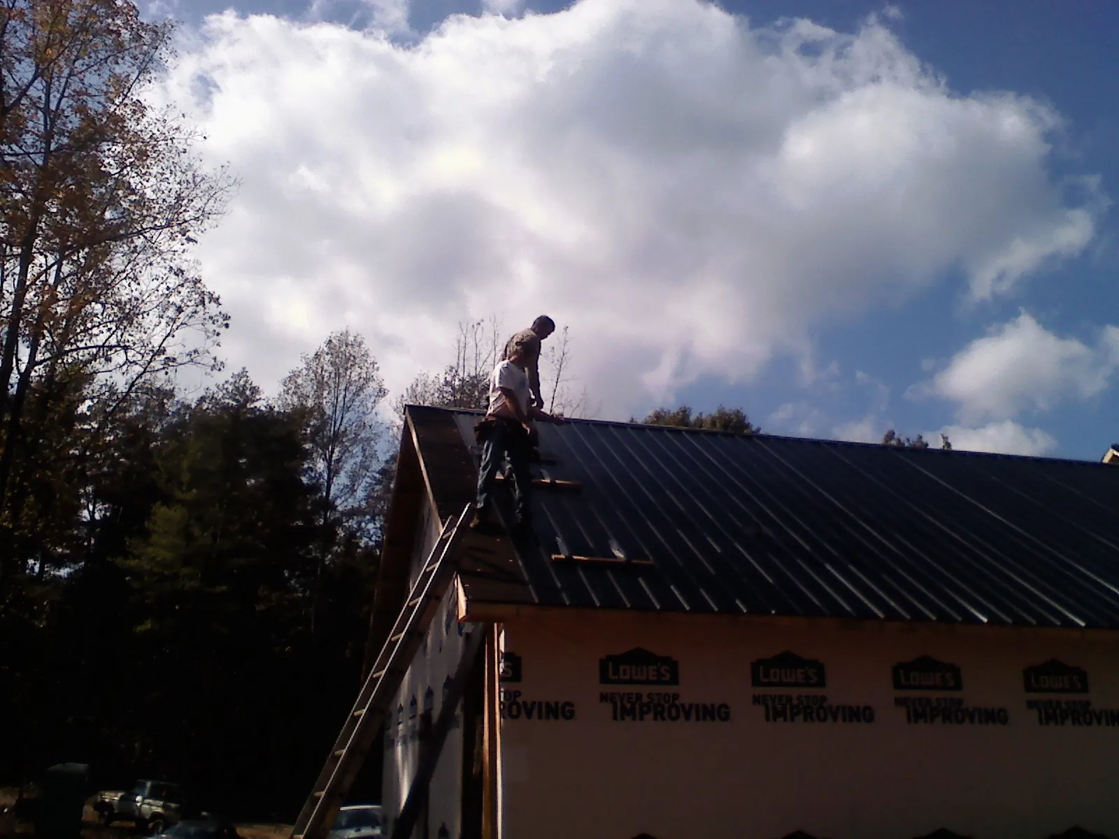 Roofer fastening dark metal panels high against a cloudy sky, from a Roof Inspection job in Cambridge