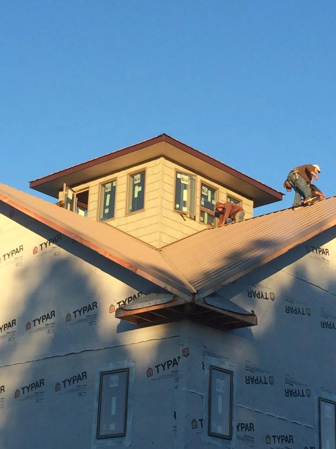 Roofers working around a rooftop cupola on a new metal roof at sunset — Roof Waterproofing in Cambridge by Roofing Brothers